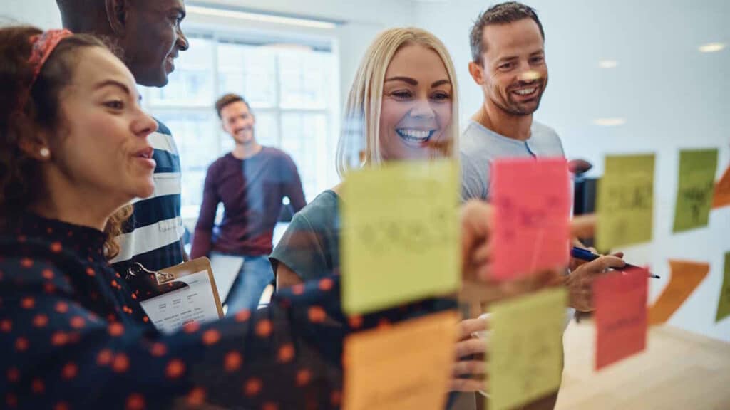 Mitarbeitende beim Brainstorming mit Haftnotizen an einer Glaswand im Büro.
