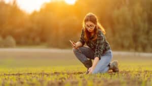 Landwirtin kniet auf einem Acker bei Sonnenschein