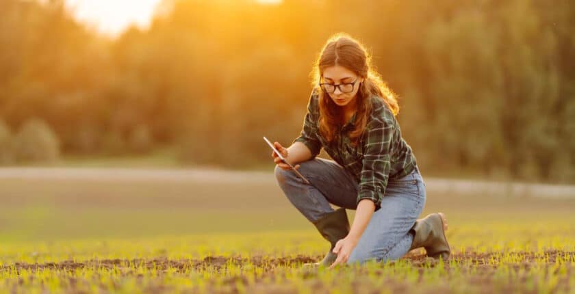 Landwirtin kniet auf einem Acker bei Sonnenschein